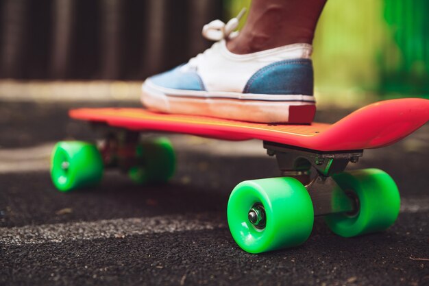 La fine dei piedi delle scarpe da tennis della ragazza guida sul pattino arancio del penny su asfalto