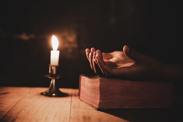 La fine sulla mano dell&#39;uomo sta pregando nella chiesa con la candela accesa