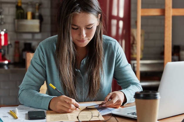 La foto dell'avvocato femminile annota il numero dal biglietto da visita nei documenti, si siede al desktop con computer portatile, telefono cellulare e documenti