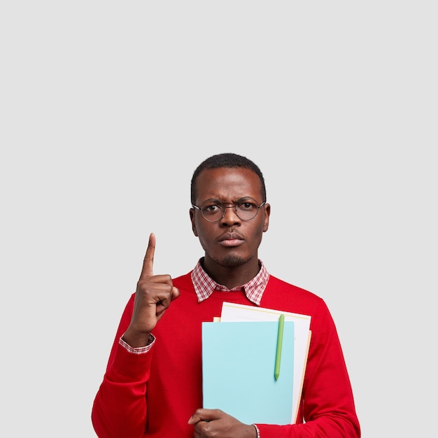 La foto dell'uomo dalla pelle scura seria ha un'espressione cupa, punti sopra, vestito in maglione rosso con la camicia, tiene il taccuino con la penna