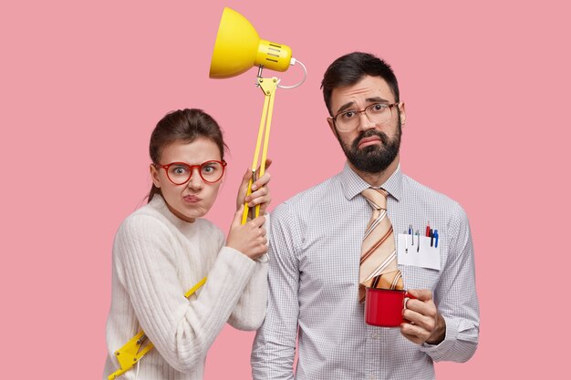 La foto della bella signora indignata con gli occhiali rossi tiene una lampada gialla, stringe le labbra, un uomo con la barba lunga scontento non ha voglia di lavorare