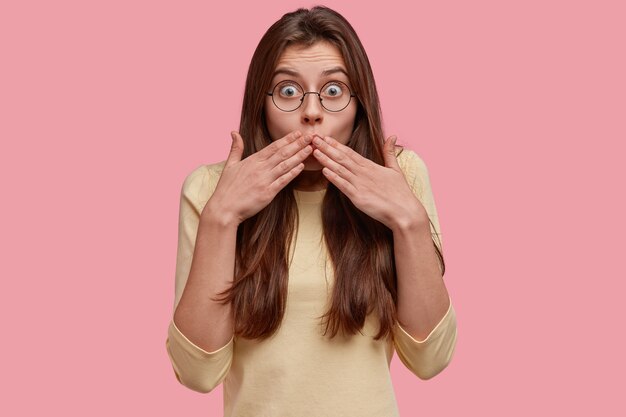 La foto della donna dai capelli scuri sorpresa copre la bocca, guarda con espressione spaventata, reagisce a qualcosa di sorprendente