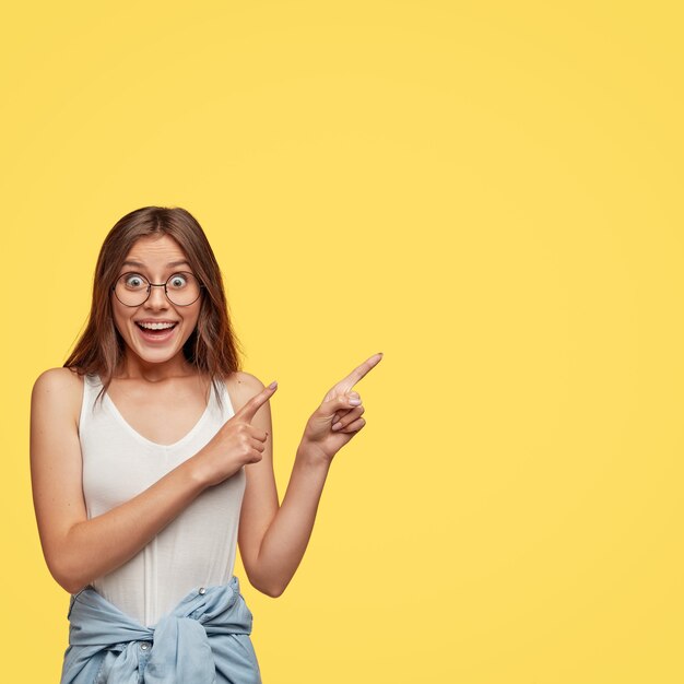 La foto della donna felice interessata guarda e indica nell'angolo in alto a destra, è fantastica