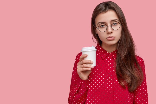 La foto della donna triste scontenta beve caffè, ha un'espressione assonnata, gode di una bevanda fresca