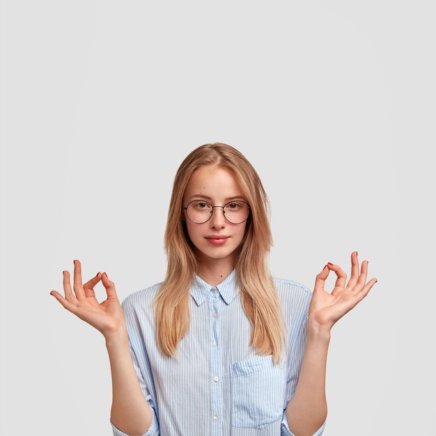 La foto della giovane femmina sicura di sé attraente fa il segno giusto con entrambe le mani, vestita in camicia elegante, mostra la sua approvazione, isolata