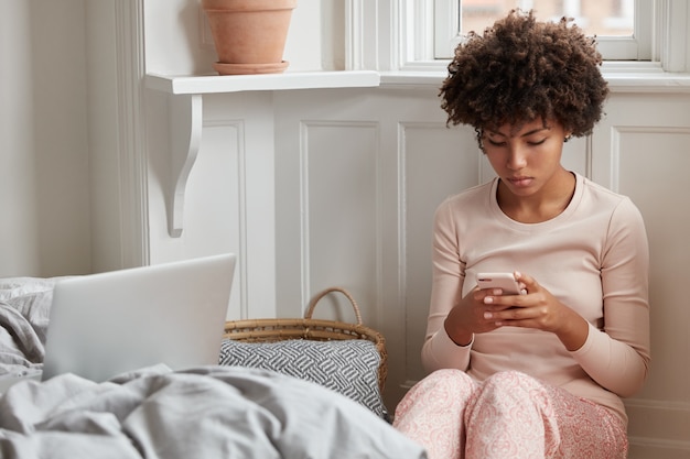 La foto della giovane femmina spensierata attraente vestita in pigiama, pubblica la posta sul telefono