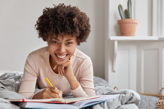 La foto della giovane signora afroamericana allegra scrive le informazioni in taccuino con la penna