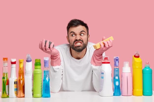 La foto di un giovane infastidito dal malcontento guarda con rabbia da parte, tiene le spugne, stringe i denti, irritata per il lavoro