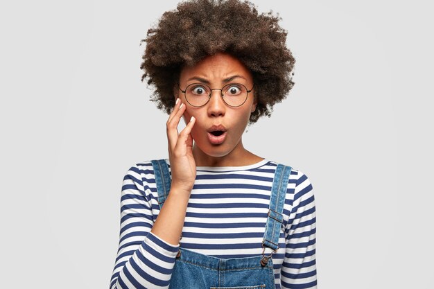 La foto di una donna afroamericana ansiosa sembra sorprendentemente e solleva le sopracciglia per lo stupore