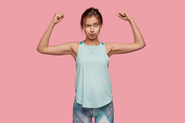 La foto di una donna sportiva sana mostra bicipiti e muscoli, alza le mani