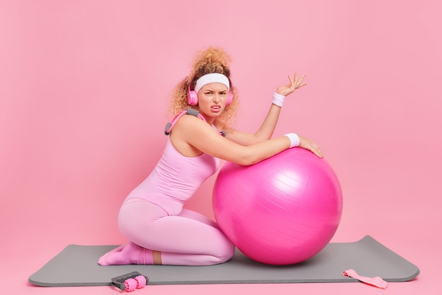 La foto orizzontale di una donna sportiva dai capelli ricci indossa braccialetti e tuta per la testa