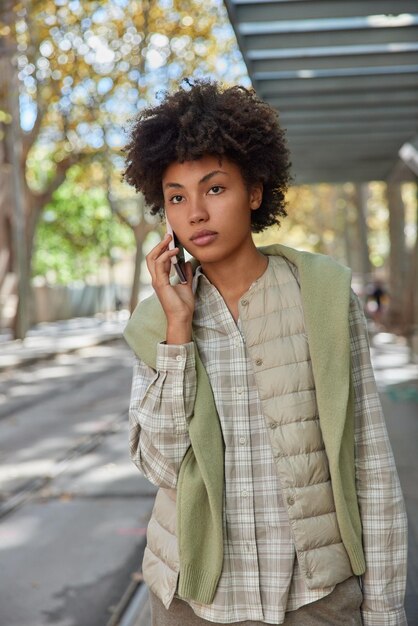 La foto verticale di una giovane donna dai capelli ricci concentrata in discorsi a distanza sul cellulare gode di una conversazione telefonica