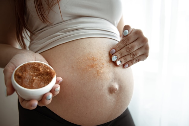 La futura mamma si strofina uno scrub naturale sulla pelle dell'addome per la cura della pelle e le smagliature.