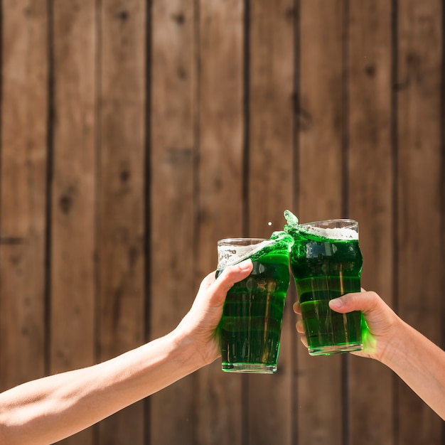 La gente che clanging i vetri della bevanda verde vicino alla parete di legno