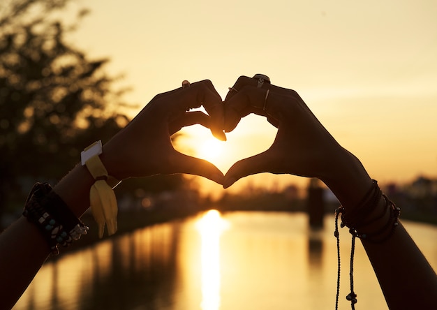 La gente che si fa le mani nel tramonto della siluetta di forma del cuore