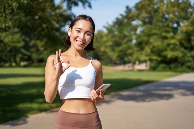 La gente di sport la sportiva asiatica felice della ragazza che mostra il segno giusto e l'allenamento sorridente in palestra dice sì appro