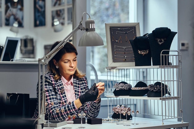 La gioielleria femminile si è vestita con abiti eleganti seduto al tavolo di lavoro e fa l'esame dei gioielli.