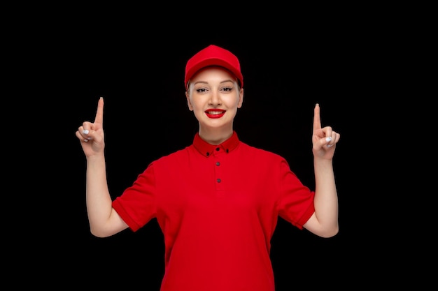 La giornata della camicia rossa ha eccitato la signora carina che punta le dita verso l'alto in un berretto rosso che indossa una camicia con il rossetto