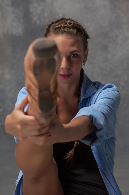 La giovane bella ballerina di stile moderno in una camicia blu in posa su uno sfondo grigio di studio. ballerina di punta a fuoco