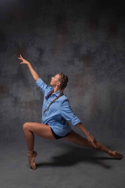 La giovane bella ballerina di stile moderno in una camicia blu in posa su uno sfondo grigio di studio