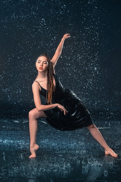 La giovane bella ballerina moderna danza sotto le gocce d'acqua