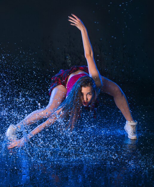 La giovane bella ballerina moderna danza sotto le gocce d'acqua