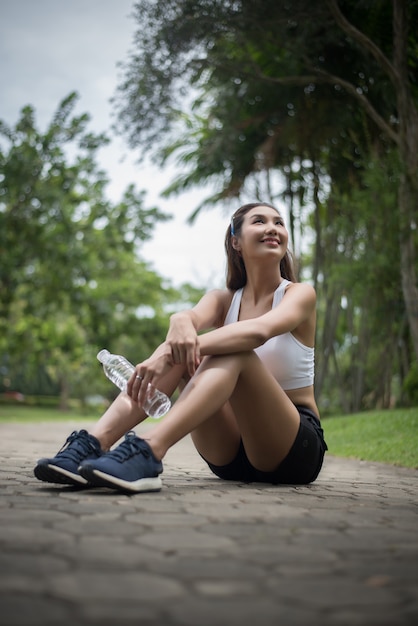 La giovane bella donna di sport si siede al parco dopo il jog. Concetto di salute e sport