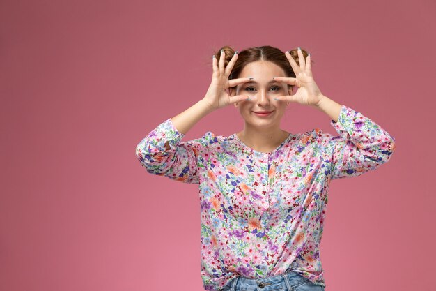 La giovane bella donna di vista frontale in fiore ha progettato la camicia e le blue jeans che sorridono mostrando i suoi occhi sulla parete rosa