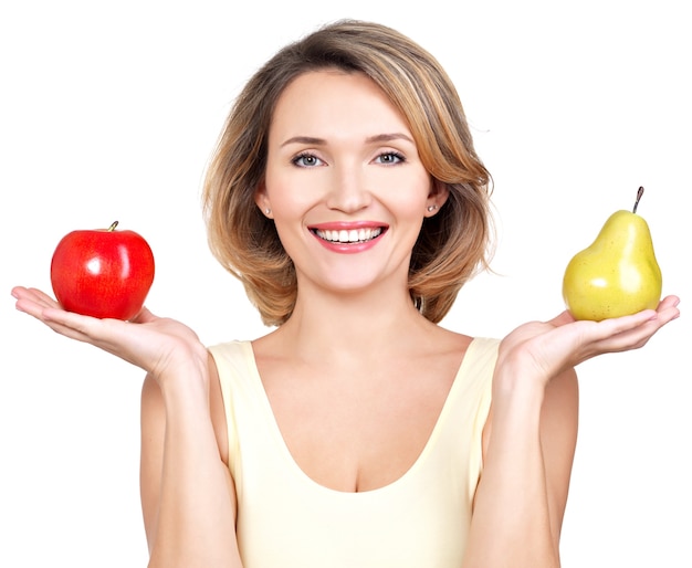 La giovane bella donna felice tiene la mela e la pera isolate su bianco.