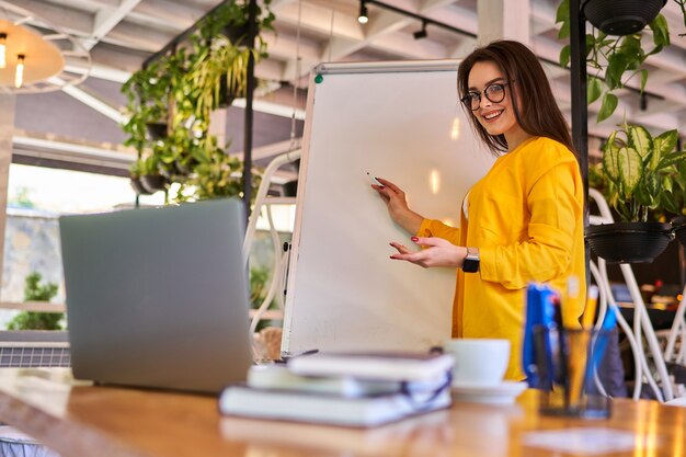 La giovane bella donna lavora in ufficio e parla in videochiamata sul laptop.