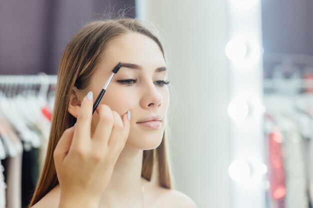 La giovane bella ragazza bionda fa un trucco naturale davanti allo specchio