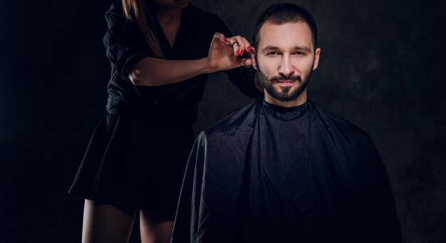 La giovane bruna attraente sta visitando un barbiere per prendersi cura della sua barba.