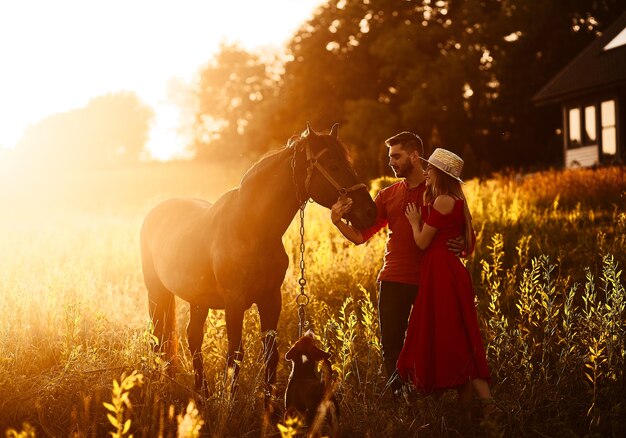 La giovane coppia affascinante sta con un cavallo marrone prima di una casa di campagna