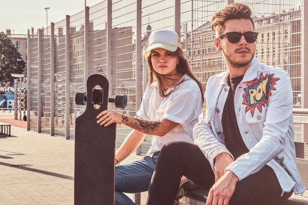 La giovane coppia alla moda si sta rilassando sulla strada soleggiata con i loro longboard. Indossano jeans.