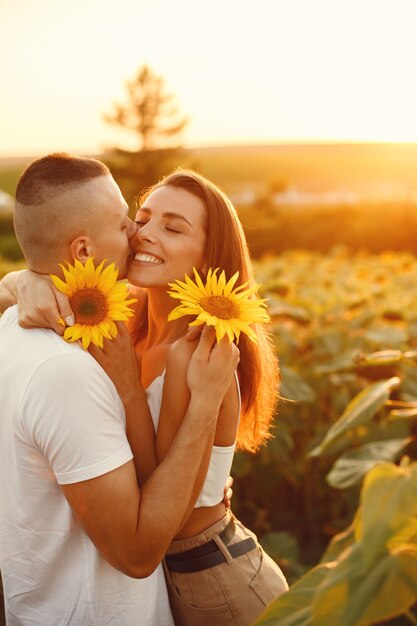 La giovane coppia amorosa sta baciando in un campo di girasoli. Ritratto di coppia in posa in estate in campo.