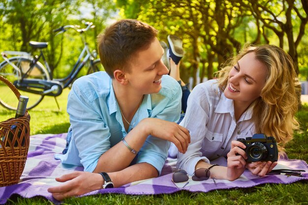 La giovane coppia attraente che utilizza una macchina fotografica compatta durante un picnic in un parco.