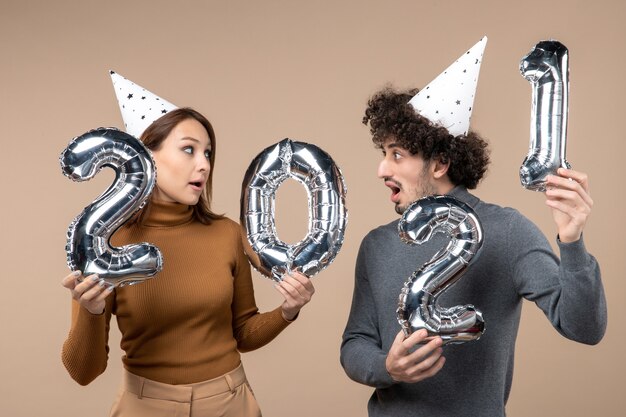 La giovane coppia sorpresa indossa le pose del cappello del nuovo anno per la fotocamera Presa della ragazza e ragazzo con e guardandosi l'un l'altro