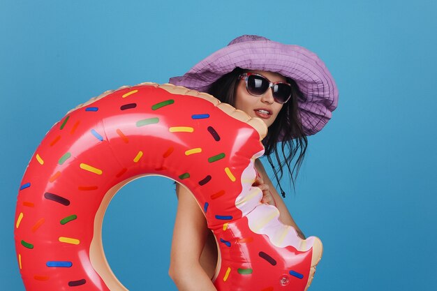 La giovane donna affascinante in cappello viola sorride posando con il grande anello di nuotata della ciambella nello studio