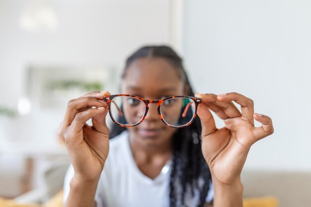 La giovane donna africana tiene gli occhiali con lenti diottriche e guarda attraverso di loro il problema della correzione della vista della miopia