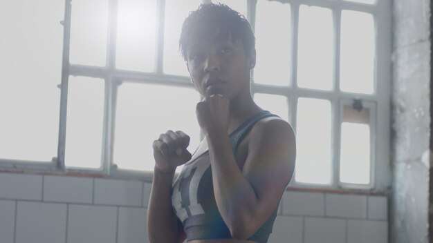 La giovane donna afroamericana di razza mista fa un allenamento di boxe in un loft soleggiato Contorno luce guardando attraverso la fotocamera