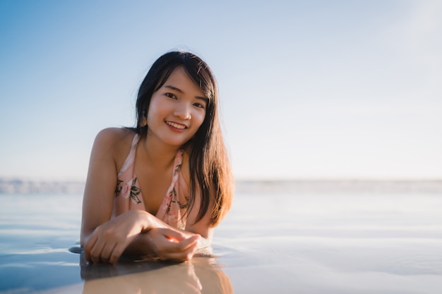 La giovane donna asiatica che ritiene felice sulla spiaggia, bella femmina felice si distende il divertimento sorridente sulla spiaggia