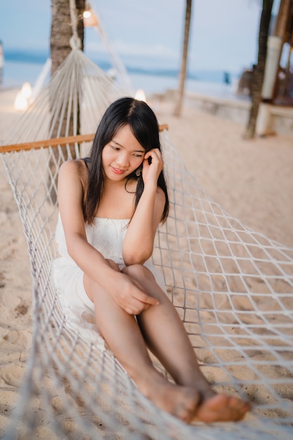 La giovane donna asiatica che si siede sull&#39;amaca si rilassa sulla spiaggia, bella femmina felice si rilassa vicino al mare.