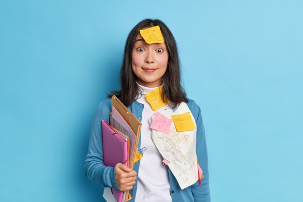 La giovane donna asiatica dai capelli scura sorpresa lavora in ufficio indossa documenti con somme scritte attaccate sui vestiti detiene cartelle vestite in maglione casual.