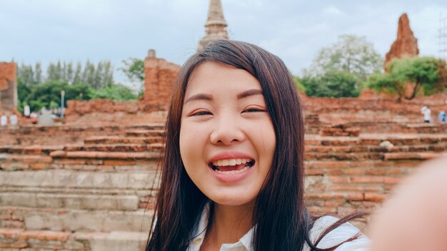 La giovane donna asiatica del blogger del viaggiatore con zaino e sacco a pelo del primo piano esamina la parte anteriore sullo smartphone