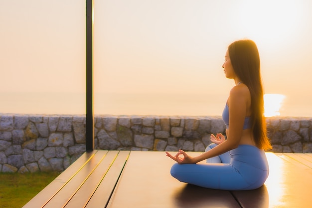 La giovane donna asiatica del ritratto fa la meditazione intorno all'oceano della spiaggia del mare all'alba