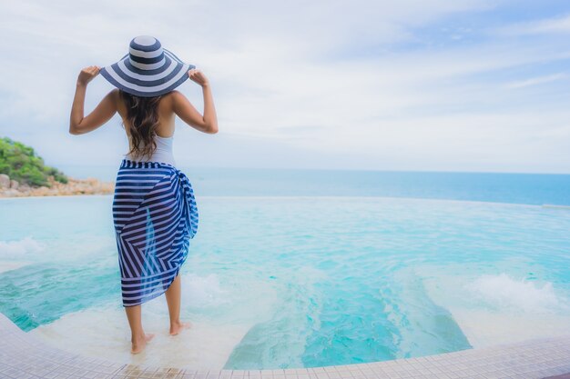 La giovane donna asiatica del ritratto si rilassa il sorriso felice intorno alla piscina all'aperto nella località di soggiorno dell'hotel con la vista di oceano del mare