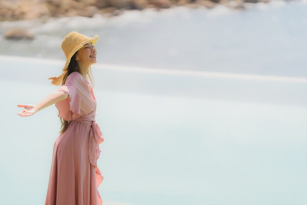 La giovane donna asiatica del ritratto si rilassa il sorriso felice intorno alla piscina all'aperto nella località di soggiorno dell'hotel con la vista di oceano del mare