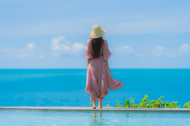 La giovane donna asiatica del ritratto si rilassa il sorriso felice intorno alla piscina all'aperto nella località di soggiorno dell'hotel con la vista di oceano del mare