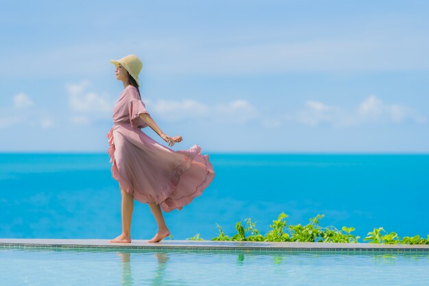 La giovane donna asiatica del ritratto si rilassa il sorriso felice intorno alla piscina all'aperto nella località di soggiorno dell'hotel con la vista di oceano del mare