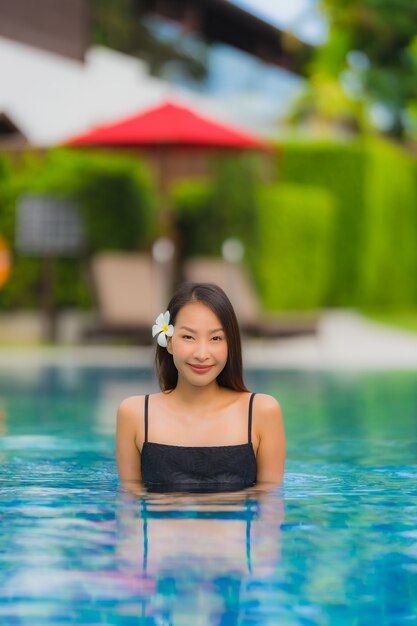 La giovane donna asiatica del ritratto si rilassa il sorriso felice intorno alla piscina all'aperto nella località di soggiorno dell'hotel con la vista di oceano del mare